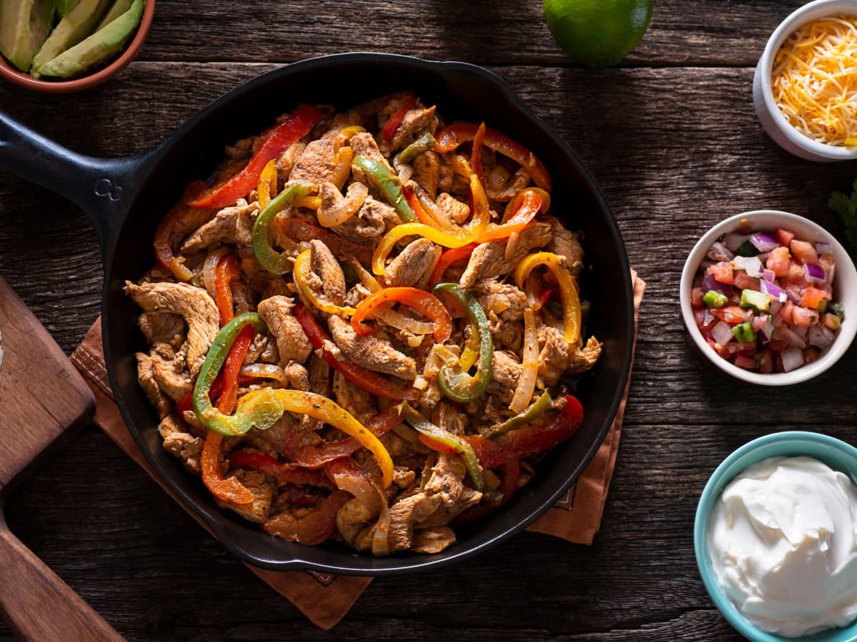 Sizzelnde Fajitas-Pfanne mit bunten Paprika, serviert mit Käse, Pico de Gallo und Sauerrahm