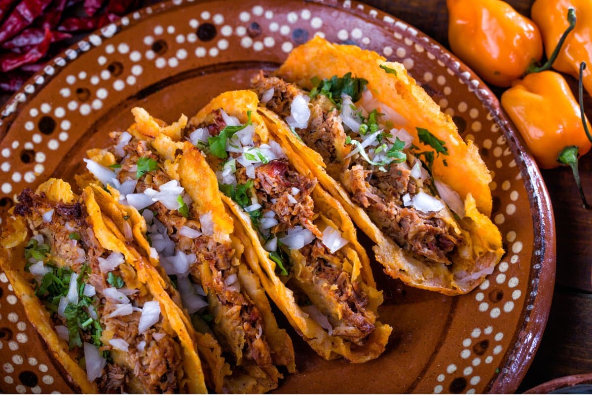 Knusprige Tacos mit geschmortem Fleisch, Zwiebeln und Koriander auf einem traditionellen mexikanischen Tonteller